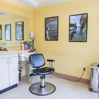 An empty hair salon with a single chair and bright yellow walls adorned with mirrors and posters.