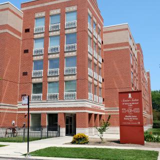 A multi-story brick residential building with a visible front entrance and surrounding greenery.