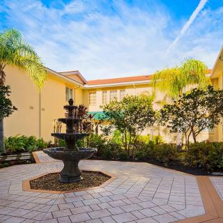 A sunny courtyard featuring a central fountain surrounded by palm trees and yellow building walls.