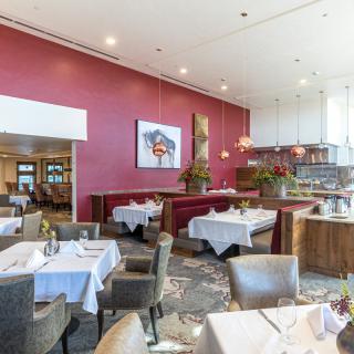 A modern restaurant interior featuring a dining area with tables and chairs, set against a vibrant red wall adorned with artwork.