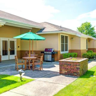 A sunny patio with a table, chairs, and an umbrella next to a grill and brick structure.