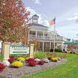 A scenic view of a building with an American flag, surrounded by colorful flowers and autumn trees.