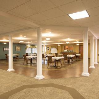 An empty dining room with tables, chairs, and columns under warm lighting.