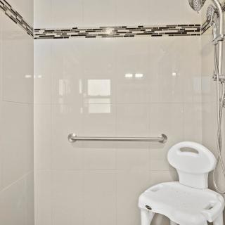 A bathroom with a shower featuring a chair and grab bar for accessibility.