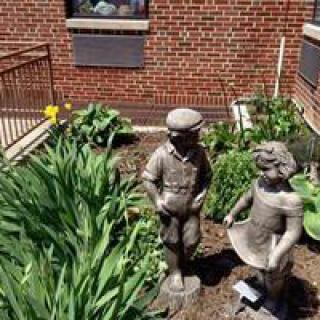 Statues of children in a garden setting next to a brick building.
