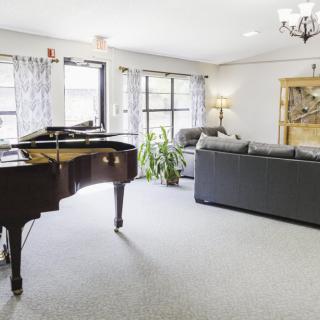 A bright and spacious living room featuring a grand piano, comfortable sofa, and large windows allowing natural light to fill the space.