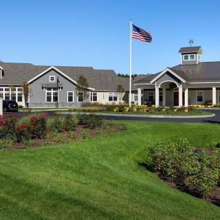 A scenic view of a building complex with well-maintained gardens and an American flag waving under a clear blue sky.