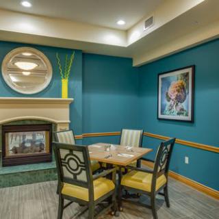 A cozy dining area with a table for four, featuring a blue accent wall, a fireplace, and decorative artwork.