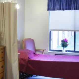 A hospital room with a single bed, dresser, and window adorned with flowers.