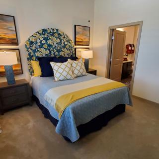 A cozy bedroom featuring a stylish bed with patterned headboard, flanked by two lamps and artwork on the walls.