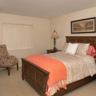 A cozy bedroom featuring a wooden bed with patterned bedding, a decorative lamp, and a patterned chair.