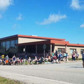 A group of people waiting outside a school building on a sunny day.