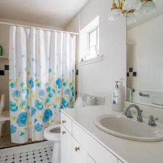 A bright bathroom with a floral shower curtain and white cabinetry.