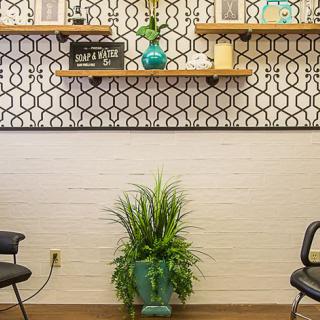 A modern waiting room with decorative shelves, a patterned wallpaper, chairs, and a potted plant.