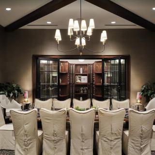 An elegant dining room with upholstered chairs and a classic chandelier, featuring a bookshelf in the background.