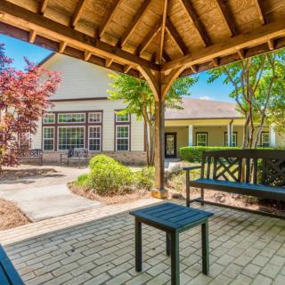 A shaded patio area with benches and a table, surrounded by a landscaped garden.