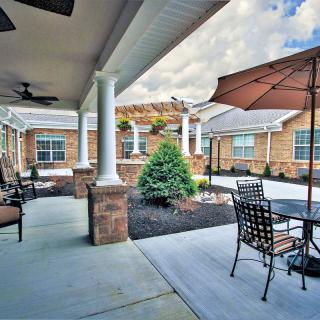 A spacious patio with outdoor seating, shaded by umbrellas, surrounded by a brick building and garden courtyard.