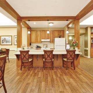 A kitchen with a central island, wooden flooring, and bar stools.