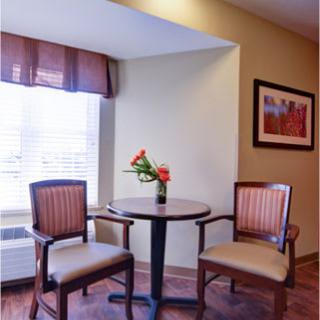 A cozy corner with a round table and two chairs, decorated with fresh flowers near a window.