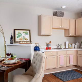 A cozy kitchen and dining area with light wooden cabinets, a small dining table set for two, and decorative elements on the countertop.