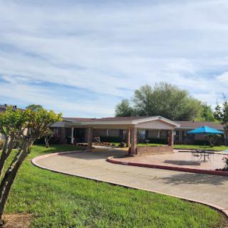 A view of a charming residential building surrounded by lush green grass and a patio area.