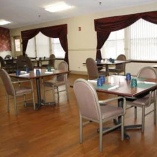 An empty dining room with neatly arranged tables and chairs, featuring a wooden floor and large windows with curtains.