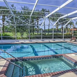 A screened outdoor pool area with a hot tub and view of palm trees.