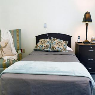 A neatly made bed with patterned pillows, a nightstand with a lamp, and a decorative chair nearby.