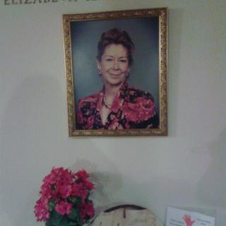 A framed portrait hanging on a wall above a table with flowers.