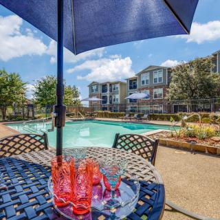 A relaxing outdoor pool area with a table and umbrella on a sunny day.
