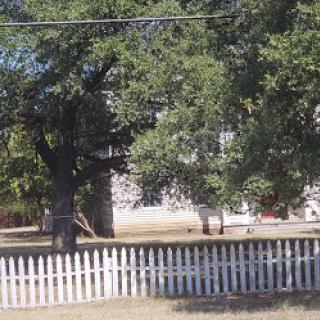 A quaint house surrounded by trees and a white picket fence.