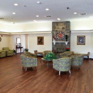 A well-lit lobby with comfortable seating around a fireplace, featuring artwork and a wooden floor.