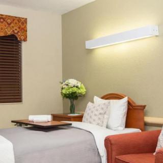 A well-lit hospital room with a neatly made bed and flowers on the bedside table.