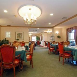 An elegant dining room with a chandelier, set for a meal with tables and red chairs.
