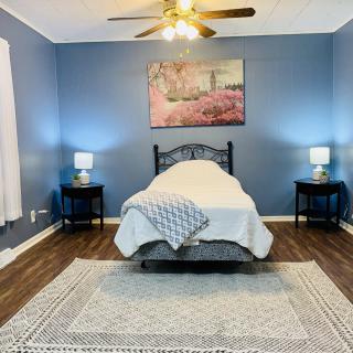 A cozy bedroom with blue walls featuring a single bed, nightstands with lamps, and a decorative wall art piece.