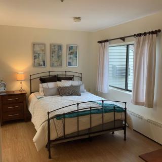 A cozy bedroom with a neatly made bed, nightstand, lamp, and artwork on the wall.