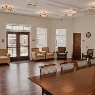 A spacious and well-lit meeting room featuring a wooden table surrounded by chairs, with comfortable seating areas for informal discussions.