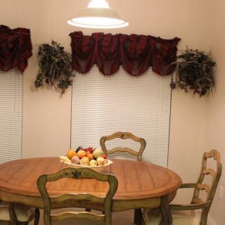 A cozy dining room with a wooden table and chairs, decorated with a fruit bowl under warm lighting.