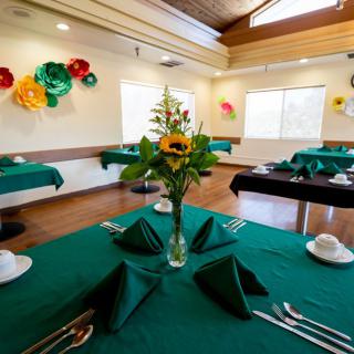 A well-decorated dining room with green tablecloths and flower centerpieces.