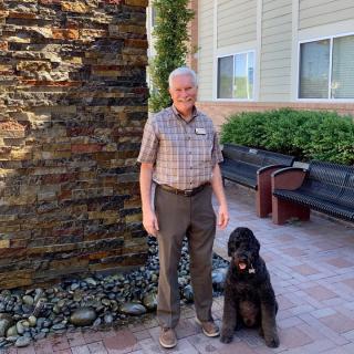 A person standing next to a large dog on a patio in front of a brick wall and building.