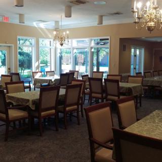 A spacious dining area with multiple tables and chairs, adorned with chandeliers and large windows allowing natural light.