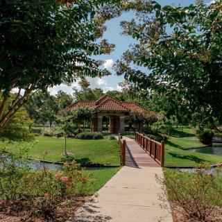 A serene garden with a wooden bridge leading to a house surrounded by lush greenery.