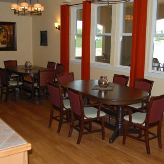 A cozy dining area with wooden tables and red chairs, accented by orange curtains and wood flooring.