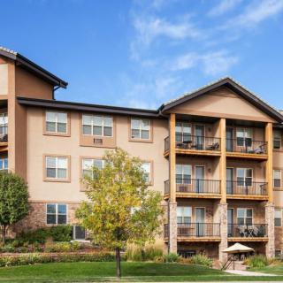 A modern apartment building with balconies and surrounding greenery under a clear blue sky.