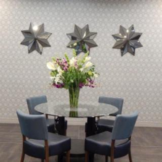 A modern dining area with a glass table, surrounded by four blue chairs and adorned with a vase of flowers, complemented by star-shaped wall decor.