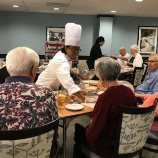 A chef serves a group of seniors at a restaurant table.