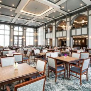 An elegant dining area with neatly arranged tables and chairs, featuring large windows and sophisticated lighting.