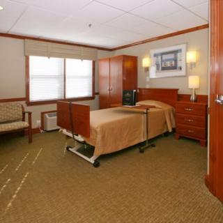 A well-furnished hospital room with a bed, cabinets, and seating area.