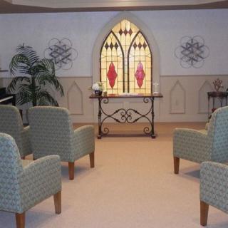 A serene chapel interior with stained glass window and arranged chairs.