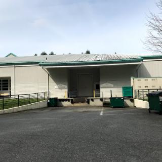 A view of an industrial building with loading docks and waste containers.